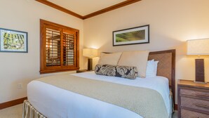 Una cama bien hecha con un almohadón estampado, un cabecero de madera, una mesita de noche con una lámpara y una ventana con persiana de madera.