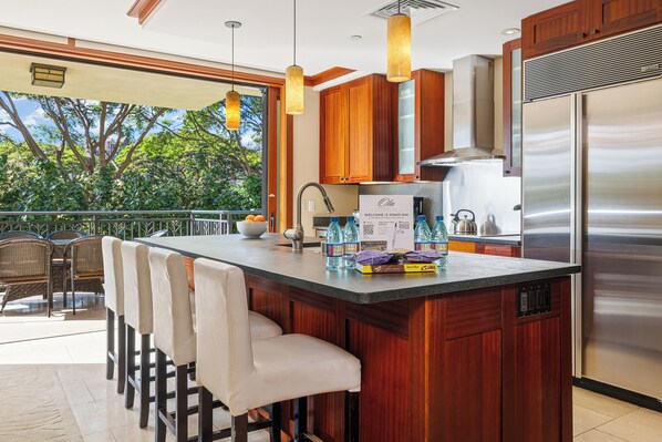 A modern kitchen with a large island, stainless steel appliances, and a view of trees.