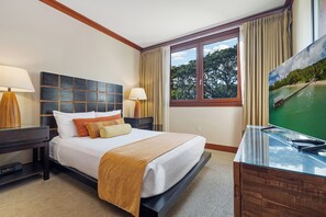 Ein Hotelzimmer mit Bett, zwei Nachttischen, einem Schreibtisch, einem Fernseher und einem Fenster mit Vorhängen.