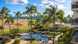 Un resort con piscina, palmeras, vista a la playa y un campo de golf.