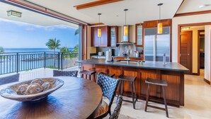 A modern kitchen with a large island, wooden cabinets, and a view of the ocean.