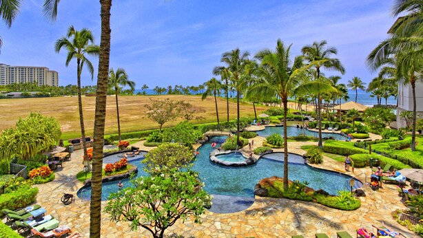 Resort com várias piscinas, palmeiras e vista para o oceano.