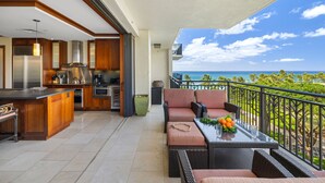 Una cocina moderna con una isla grande, un comedor con mobiliario de mimbre y un balcón con vista al océano.
