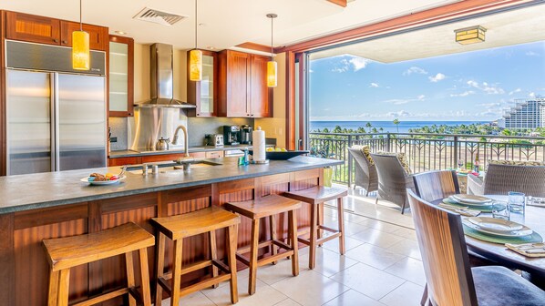 A modern kitchen with a large island, bar stools, and a view of the ocean.