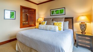 A neatly made bed with a patterned bedspread, two bedside lamps, and a window with wooden shutters.