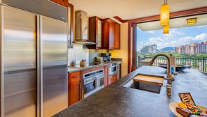 A modern kitchen with stainless steel appliances, wooden cabinets, and a large window overlooking a cityscape.