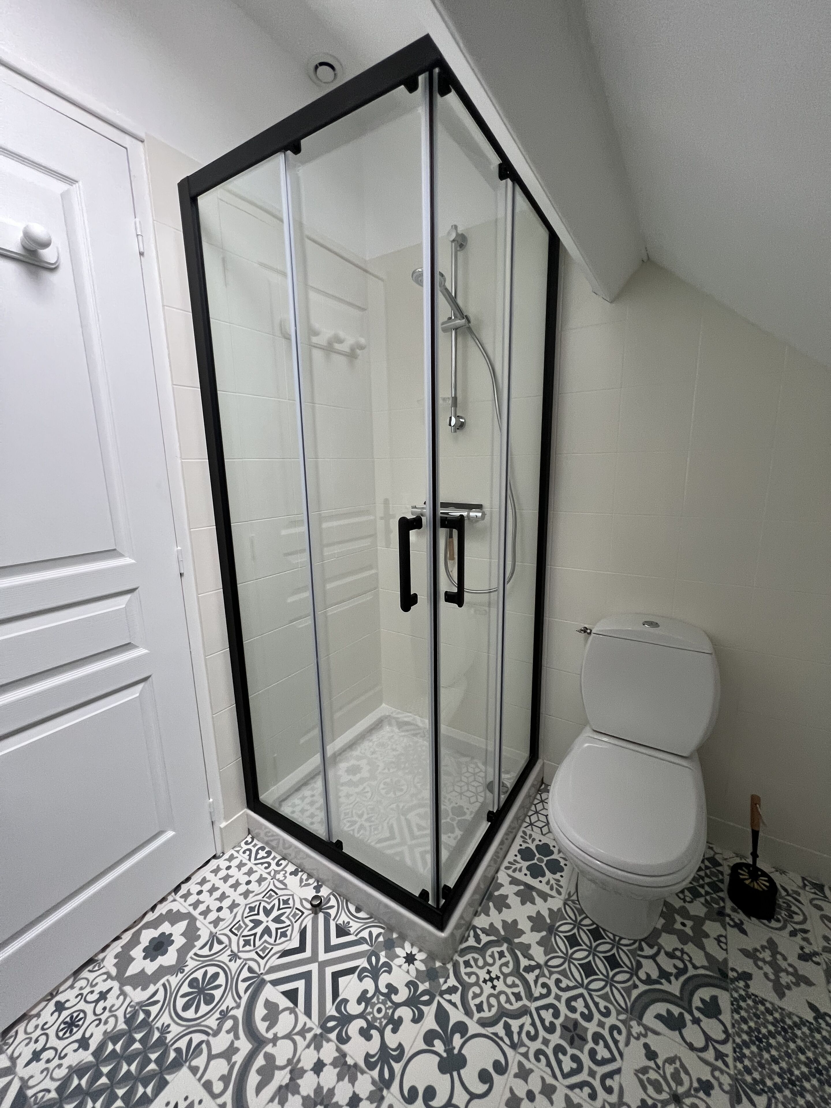 Une salle de bain avec une douche à parois de verre, des toilettes blanches et un carrelage au sol à motifs.