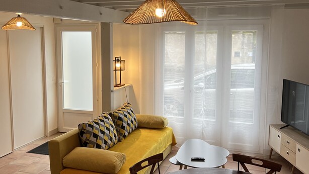 A living room with a yellow sofa, a wooden dining table, and two pendant lights. - Charmante Maison en Brenne (Vendœuvres)