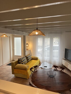 Un salon avec un canapé jaune, une table à manger en bois et deux lampes suspendues.