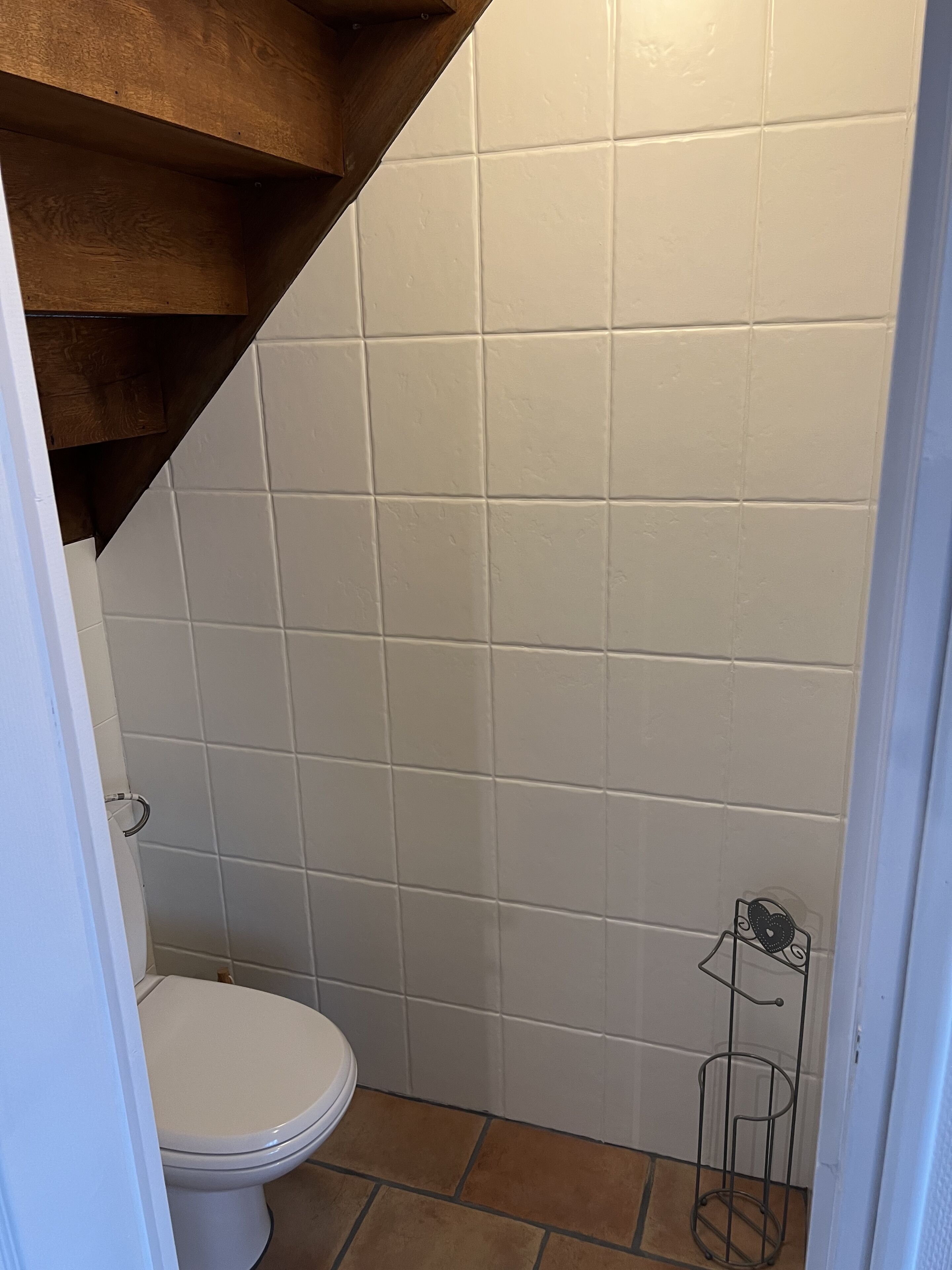 Een kleine badkamer met witte tegels, een wit toilet en een metalen rek.