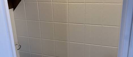 Een kleine badkamer met witte tegels, een wit toilet en een metalen rek.