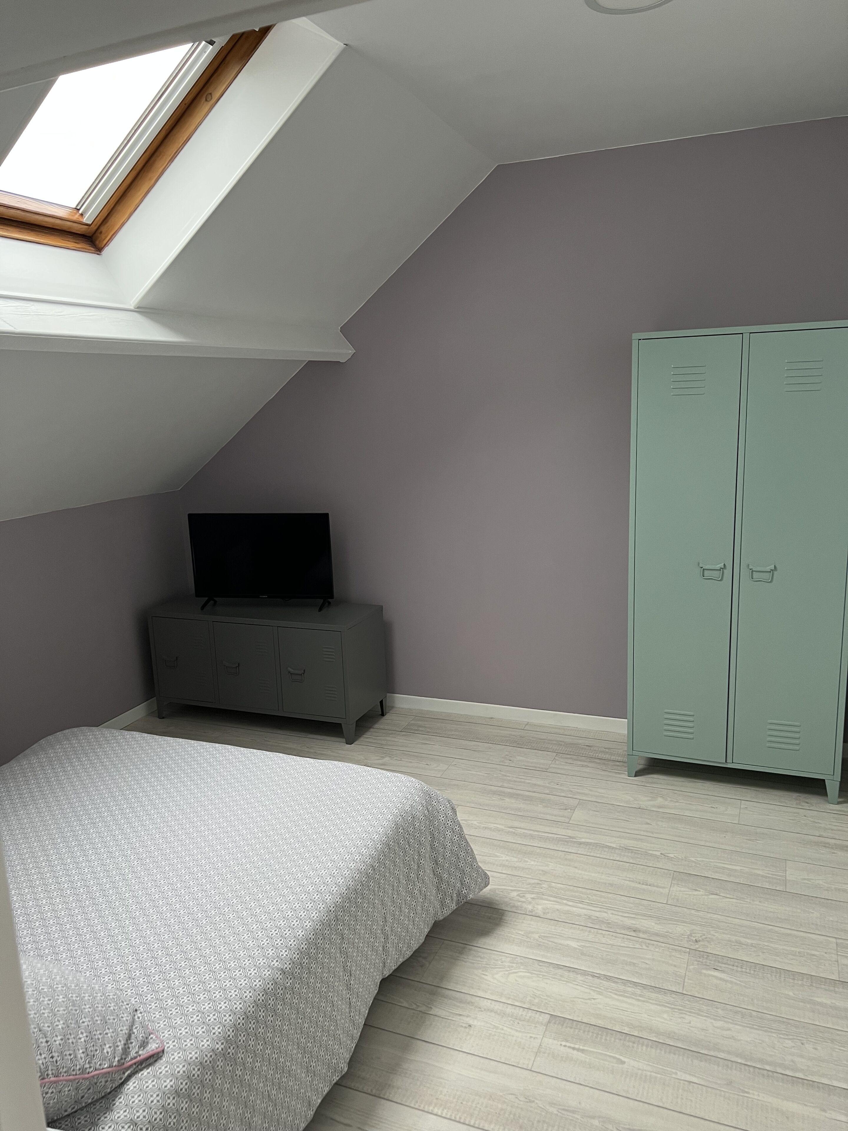 A bedroom with a sloped ceiling, a bed, a wardrobe, and a television on a cabinet.