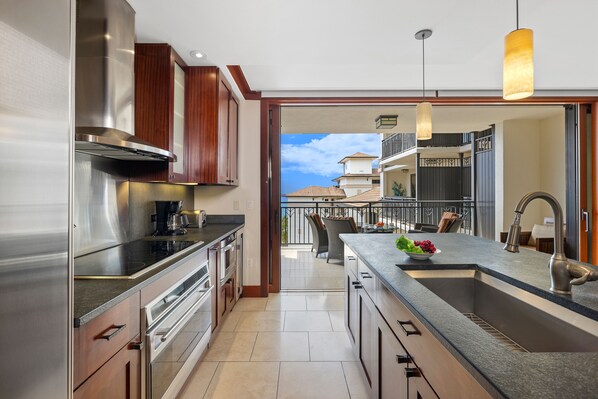 A modern kitchen with stainless steel appliances, a large island with a sink, and a view to a balcony.