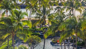 A tropical resort with a pool area surrounded by palm trees, overlooking the ocean.