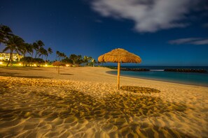 Una playa con un quiosco de paja, palmeras y un hotel al fondo.