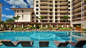 Área de piscina de hotel com espreguiçadeiras e um edifício grande ao fundo.