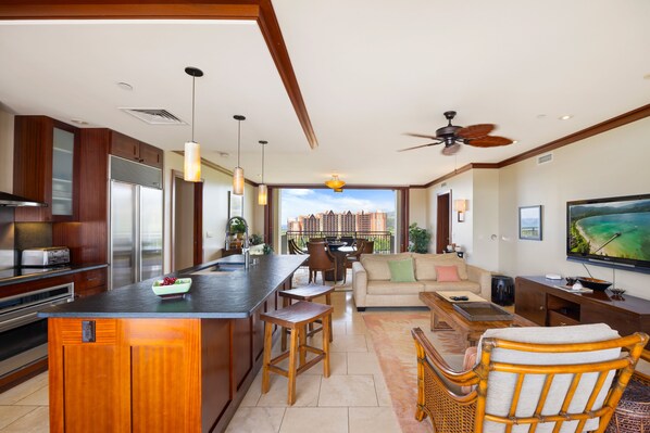 Una cocina moderna con una isla central, un comedor con vistas y una sala de estar con televisor.