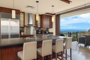 A modern kitchen with a large island, bar stools, and a view of the ocean.