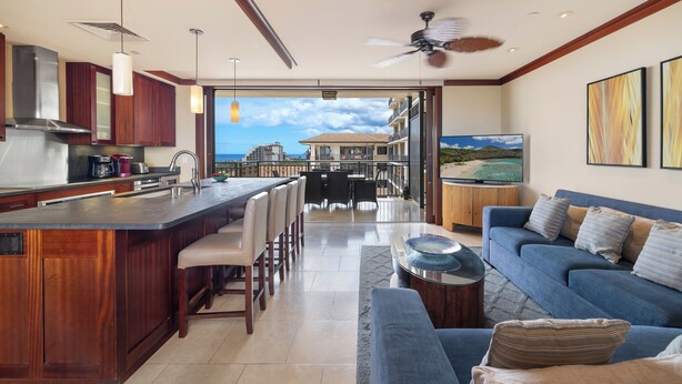 A modern kitchen with a bar area, dining space, and a living area with a sofa and TV. - Ko Olina Beach Villas O1121: Luxurious Villa w/Golf Course & Ocean Views (Kapolei)