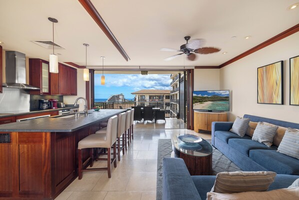 A modern kitchen with a bar area, dining space, and a living area with a sofa and TV.