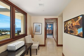 A hallway with a view of the ocean, a framed picture, a printer, and a dining area in the background.