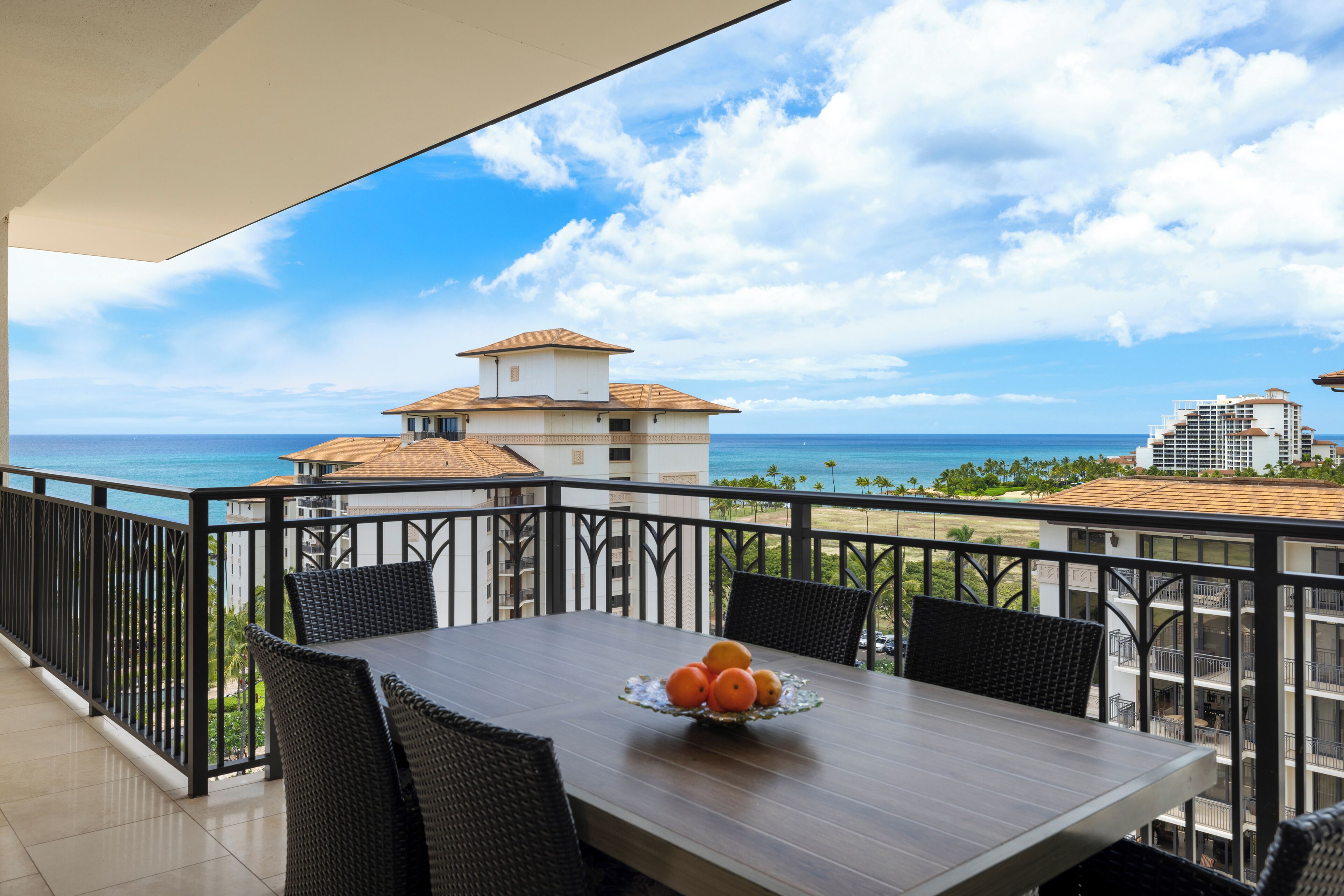 A balcony with a dining table, chairs, and a fruit bowl.