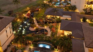 Un resort con piscina, palmeras y vistas al océano al atardecer.