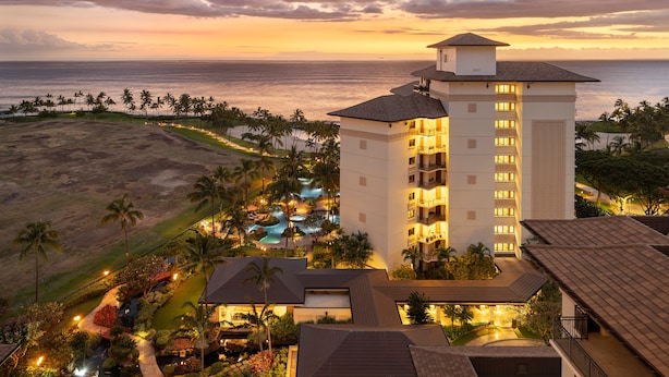 Un resort con piscina, palmeras y vista al océano al atardecer.