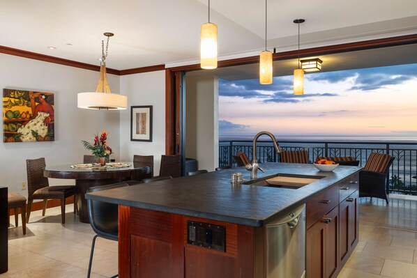 A modern kitchen with a large island, pendant lights, and a view of the ocean.