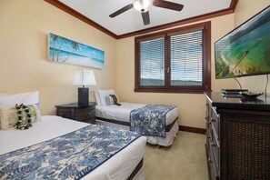 A hotel room with two beds, a ceiling fan, a large window with blinds, a TV, and artwork on the walls.