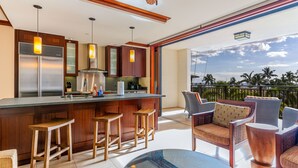 Una cocina moderna con barra, taburetes de madera y vista a palmeras.