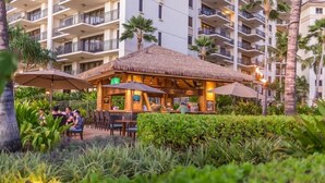 Un restaurante con techo de paja, mesas al aire libre, rodeado de exuberante vegetación y palmeras.