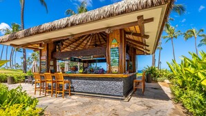 Un bar frente a la playa con techo de paja, sillas de madera y una barra de piedra.