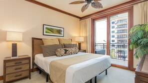Une chambre d’hôtel avec un lit, deux tables de chevet, un ventilateur de plafond, une grande fenêtre donnant sur un immeuble et une plante en pot.