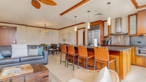 A modern kitchen with wooden cabinets, a stainless steel range hood, and a bar area with bar stools. - Ko Olina Beach Villas O425: Oceanfront Getaway (Kapolei)