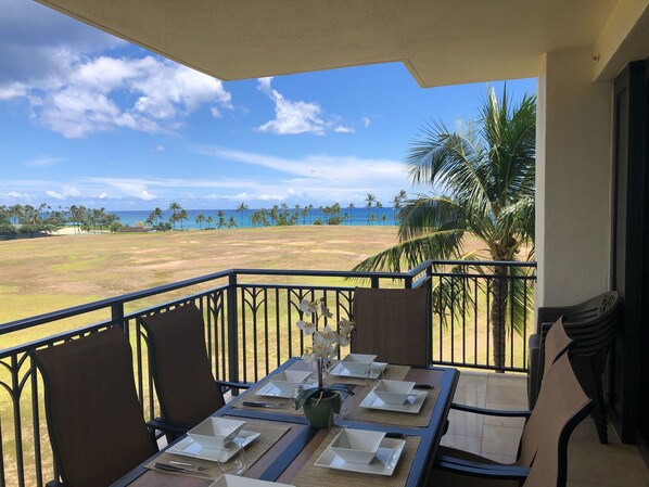 Ein Balkon mit Esstisch, der auf einen Strand mit Palmen und den Ozean hinausblickt.