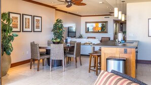 Una cocina moderna con una isla central, comedor con sillas de mimbre y sala de estar con sofá y televisor.