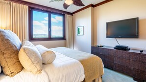 Habitación de hotel con una cama grande, un televisor de pantalla plana, un armario de madera y una ventana con cortinas.
