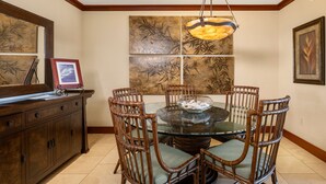A dining area with a glass table surrounded by wicker chairs, a wooden cabinet, and a large wall art piece.