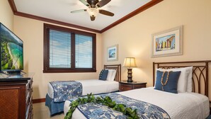 A hotel room with two beds, a ceiling fan, a window with blinds, a desk with a lamp, and artwork on the walls.