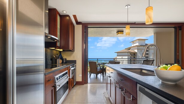 A modern kitchen with stainless steel appliances, wooden cabinets, and a large island with a bowl of fruit. - Ko Olina Beach Villas O805: Chef's Kitchen & Stunning Views (Kapolei)