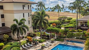 A swimming pool with lounge chairs, palm trees, and a building in the background. - Ko Olina Beach Villas O805: Chef's Kitchen & Stunning Views (Kapolei)
