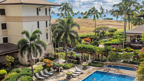 A swimming pool with lounge chairs, palm trees, and a building in the background.