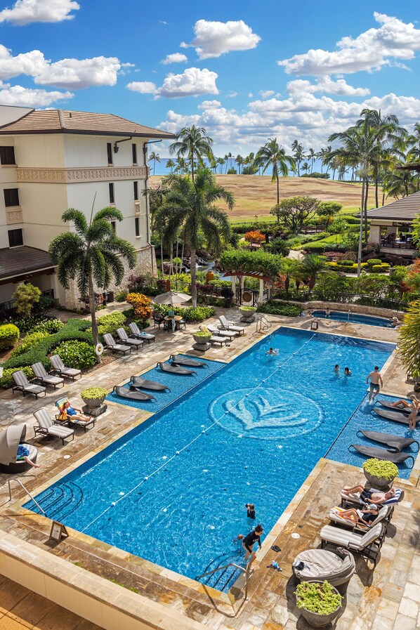 A swimming pool with lounge chairs, palm trees, and a building in the background. - Ko Olina Beach Villas O805: Chef's Kitchen & Stunning Views (Kapolei)