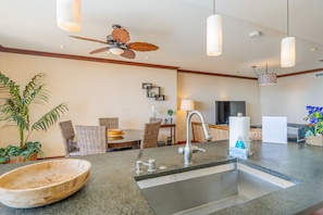 A modern kitchen with a granite countertop, stainless steel sink, and a ceiling fan.