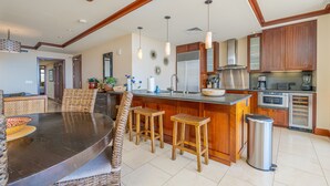 A spacious kitchen with a central island, wooden bar stools, a dining table with chairs, and modern appliances.