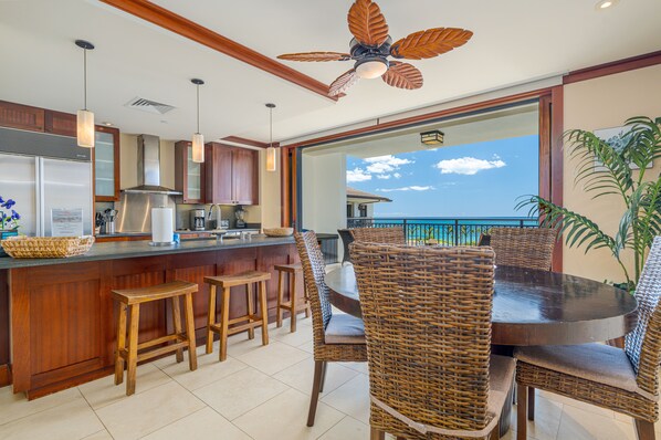 A modern kitchen with a bar area, wicker furniture, and a view of the ocean.