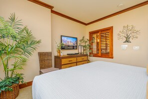 A bedroom with a large bed, a television on a dresser, and a window with wooden shutters.