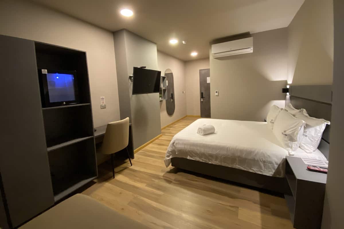A modern hotel room with a bed, a desk, a chair, a TV, and an air conditioning unit.