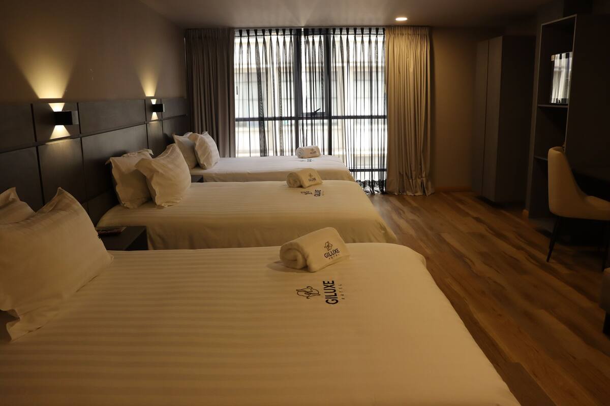 A hotel room with two beds, each with a pillow and a towel with the hotel logo. There is a bookshelf and a chair in the room.